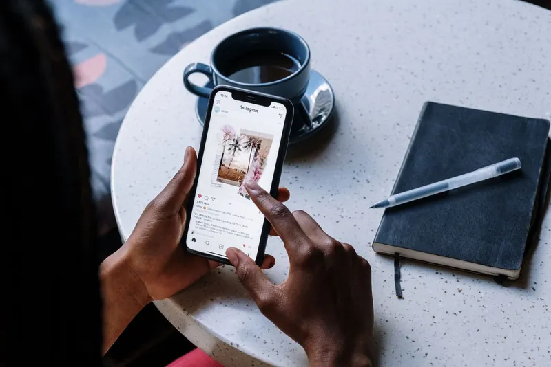 Hands holding a smartphone above a café table with coffee and a notebook