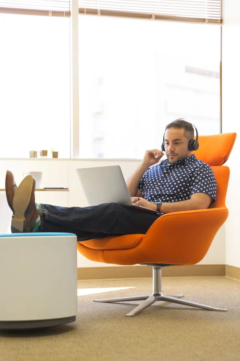 A man using a laptop and headphones in an orange chair