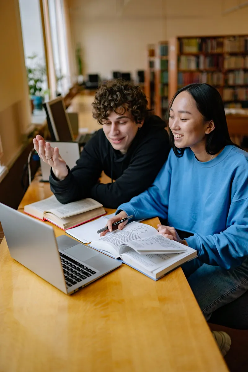 Two adults working with books and a laptop in a library
